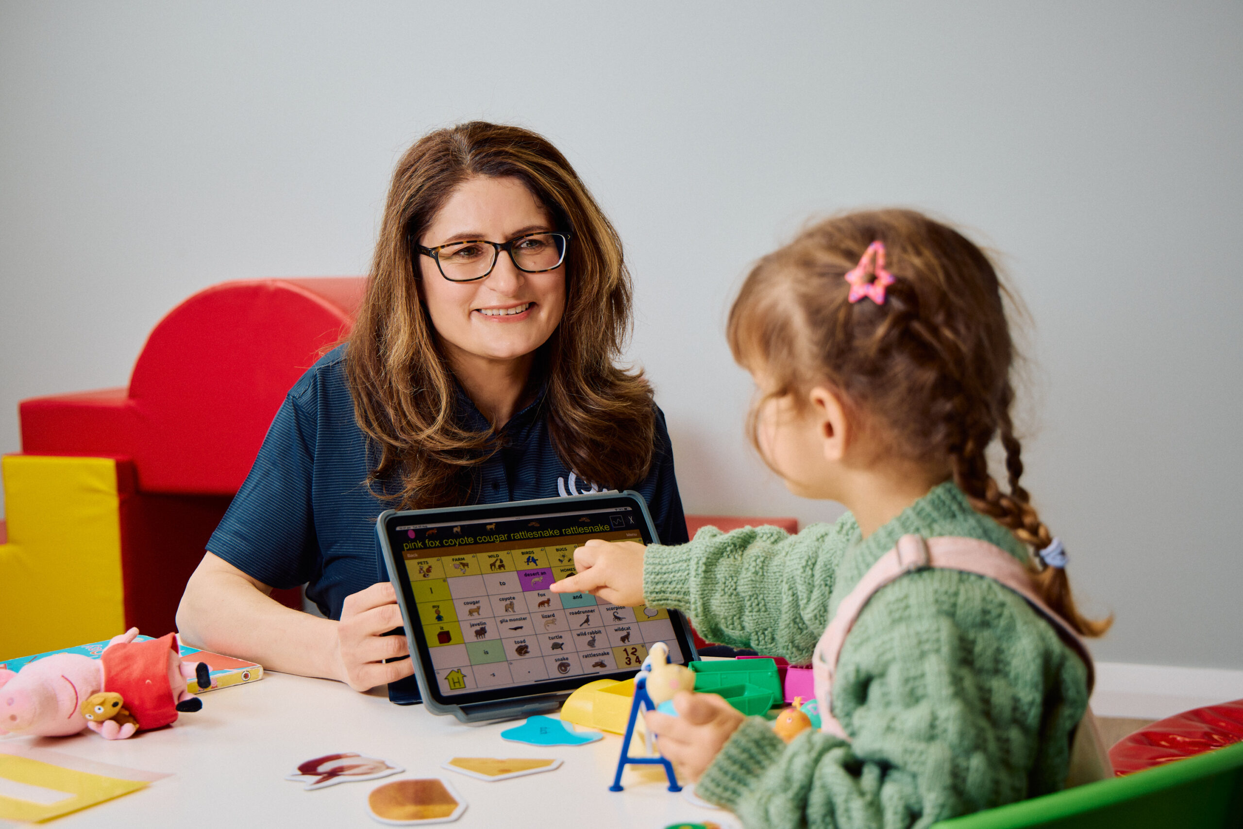 Speech pathologist is communicating with a young female child using a communication device.